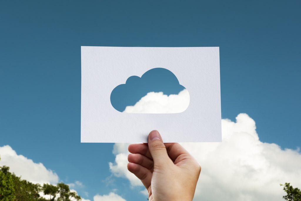 A hand holding a cut-out of a cloud up to a cloud in the sky, symbolizing off-site backups.